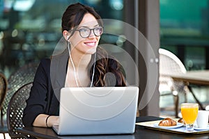 Beautiful young woman looking sideways while working with her laptop in a coffee shop.