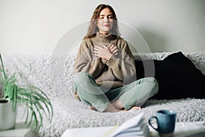 Beautiful young woman in lotus pose on bed practicing pranayama breathing techniques, finding inner balance after a