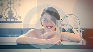 Beautiful young woman lying in the bath and holding a glass of c