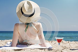 A beautiful young woman lying on the beach next to a martini cocktail