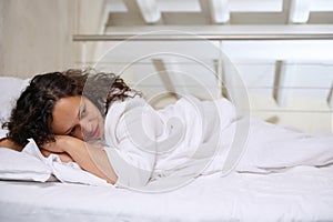 Beautiful young woman lying in bed while covered with soft blanket, falling sleep in bed at home bedchamber