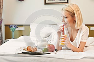Beautiful young woman lying on bed and having breakfast