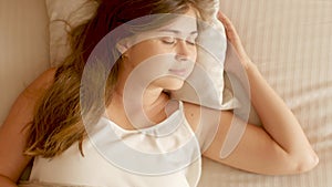 Beautiful young woman lying in bed and sleeping on pillow, girl resting, awakening at sunny morning, top view