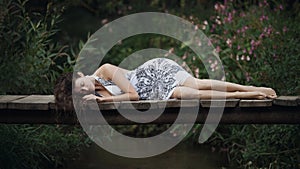 Beautiful young woman lying on the bridge over the forest river.