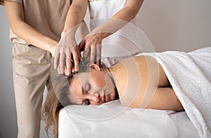 Beautiful young woman lying with closed eyes and having head massage at spa in four hands. masseur student massage