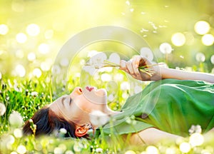 Beautiful young woman lying on the field in green grass and blowing dandelion flowers