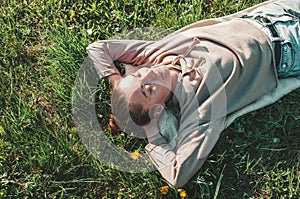 Beautiful Young Woman lying on a field, green grass and dandelion flowers. Outdoors Enjoy Nature. Healthy Smiling Girl lying in photo