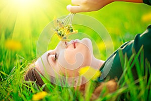 Beautiful young woman lying on the field in green grass and smelling blooming dandelions. Allergy free