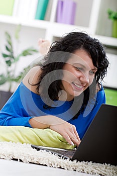 beautiful young woman lying on the floor at home with laptop,typing