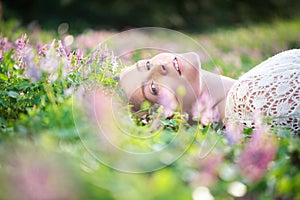 Beautiful young woman lying on grass with spring flowers