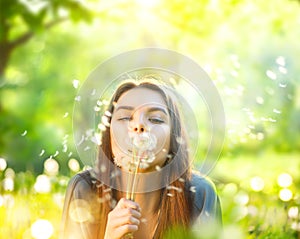 Beautiful young woman lying on green grass and blowing dandelions
