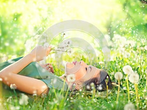 Beautiful young woman lying on green grass and blowing dandelions photo