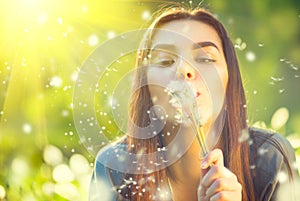 Beautiful young woman lying on green grass and blowing dandelions