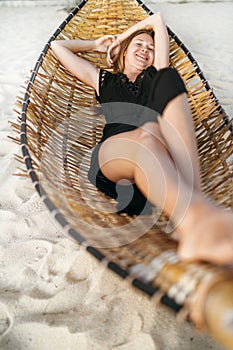 Beautiful young woman lying in hammock on the sandy beach and cheerful smiling in camera top view