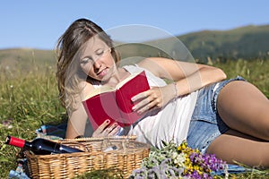 Beautiful young woman lying on a meadow, reading book, next to p