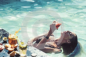 Beautiful young woman lying in water with a cocktail in her hands.