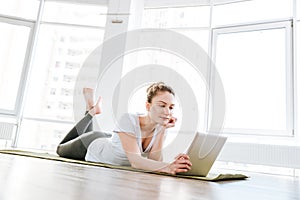 Beautiful young woman lying on yoga mat and using tablet