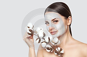 A beautiful young woman makes a moisturizing mask on her face, she is holding a cotton flower in her hands