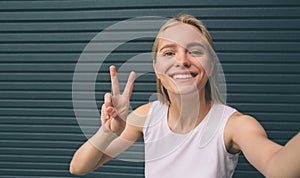 Beautiful young woman making self-portrait on a smartphone on a wall background.