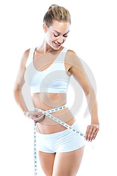 Beautiful young woman measuring her slim body over white background.