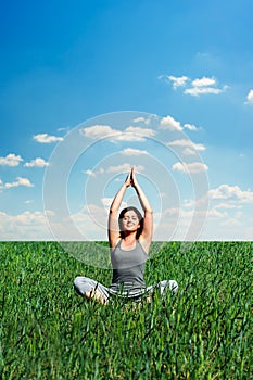 Beautiful young woman meditating at the meadow