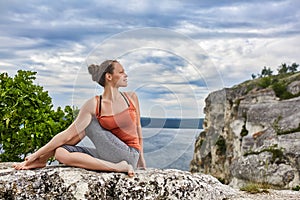 Beautiful young woman meditating in yoga pose at a big river against dramatic sky.