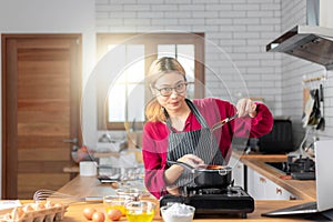 Beautiful young woman is mixing batter, looking at camera and smiling while baking in kitchen at home ,decorating a cake of