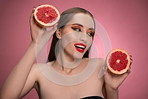 Beautiful young woman model holding two juicy grapefruit sliced in half in her hands looking sideways. Charming joyful