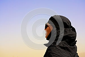 Beautiful young woman model portrait with sunglasses in black abaya with creal blue sky