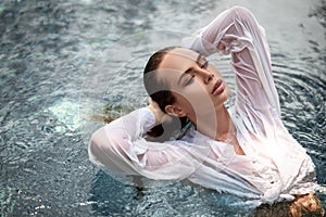 Beautiful young woman model in white shirt posing in the pool.