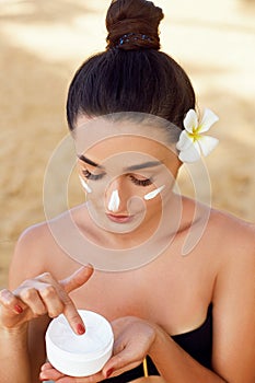 Beautiful Young woman with moisturizing  cream on face. Girl holding bottle   cosmetic cream. Female applying  lotion on skin.