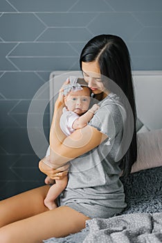 Beautiful young woman mother holds her daughter in her arms, looks at her and smiles at her