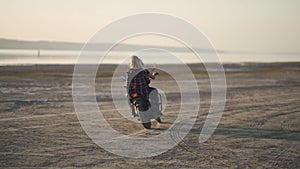 Beautiful young woman motorcyclist with his girlfriend riding a motorcycle in a desert on sunset or sunrise. Girlfriends on a bike