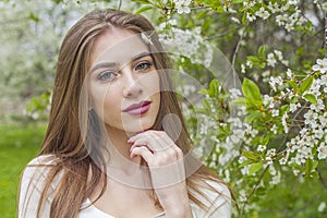 Beautiful young woman with natural makeup and healthy long brown hair in blossom park outdoors. Natural female beauty portrait