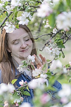 Beautiful young woman near blossoming apple tree enjoys the aroma of flowers. Portrait of girl in the spring garden. Vertical