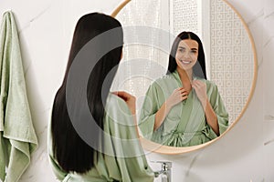 Beautiful young woman near mirror in bathroom