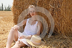 Beautiful young woman near rolled hay bale on sunny day