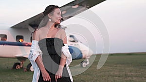 Beautiful young woman next to the plane. Portrait of a beautiful smiling woman in a hat and black dress. young woman in