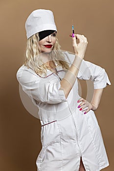 Beautiful young woman in nurse uniform with a syringe in her hand and a black eye patch. Sexy blonde with red lips. Compulsory