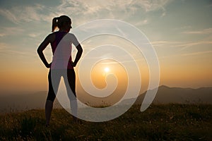 Beautiful young woman observing sunset after running on a mountian