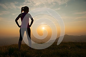 Beautiful young woman observing sunset after running on a mountian photo