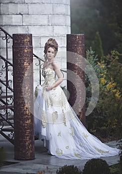 Beautiful woman in an old medieval dress, with a high complex historical hairstyle near the walls of the castle.