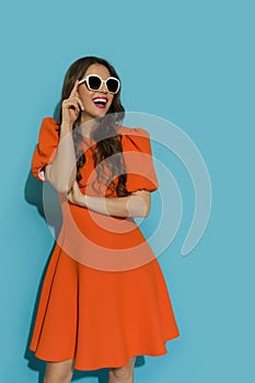 Beautiful young woman in orange cocktail dress and sunglasses is looking away and laughing
