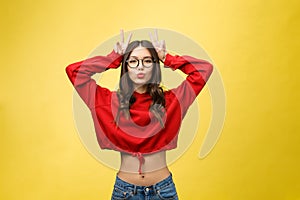 Beautiful young woman over isolated yellow background Posing funny and crazy with fingers on head as bunny ears, smiling