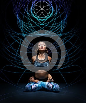 Beautiful young woman in padmasana pose. Colorful mandala on black background behind