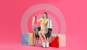 Beautiful young woman with paper shopping bags in armchair on pink