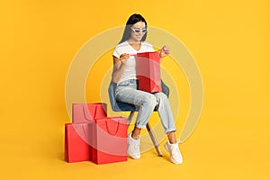 Beautiful young woman with paper shopping bags in armchair on yellow background