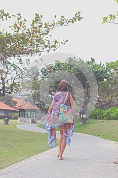 Beautiful young woman in pareo and swimsuit walking in the becah park with bag on sunny summer day. Tropical island Bali
