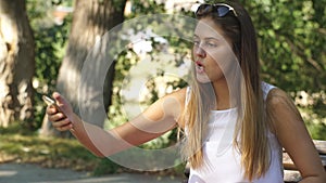 Beautiful young woman on a Park bench taking a selfie