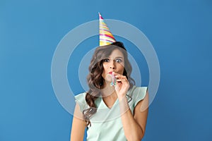 Beautiful young woman with party whistle and cap on color background